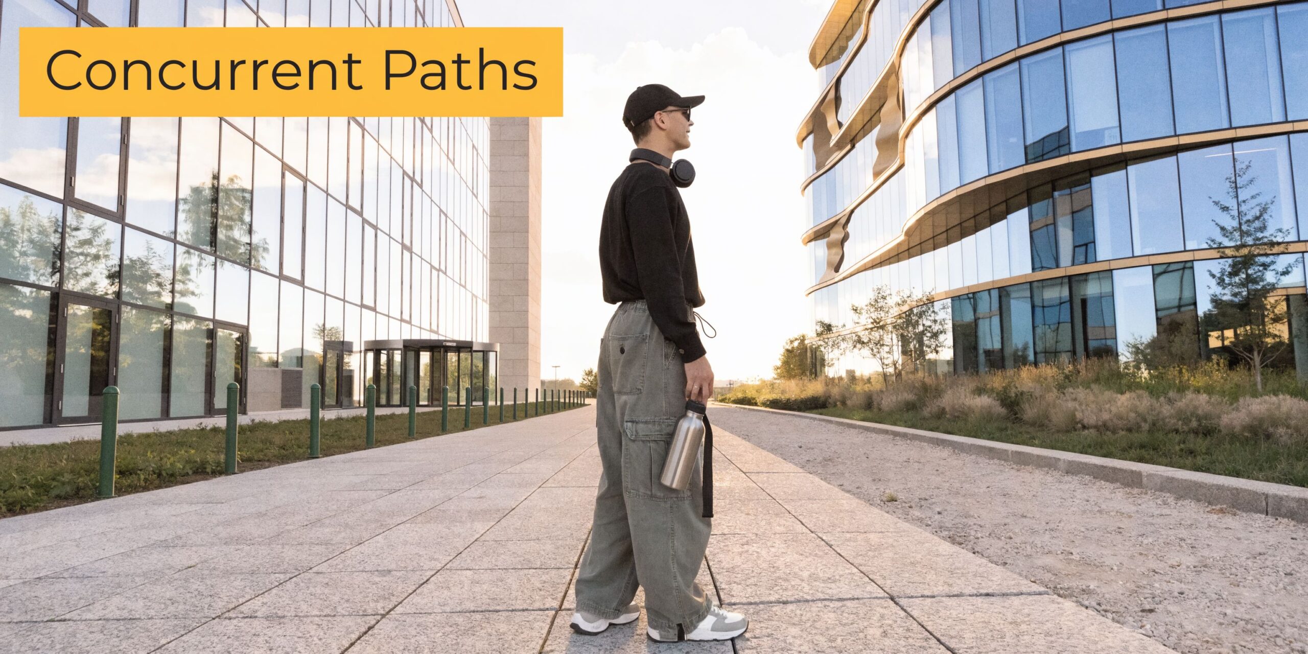 A person standing on a walkway between two modern office buildings, holding a reusable metal water bottle.