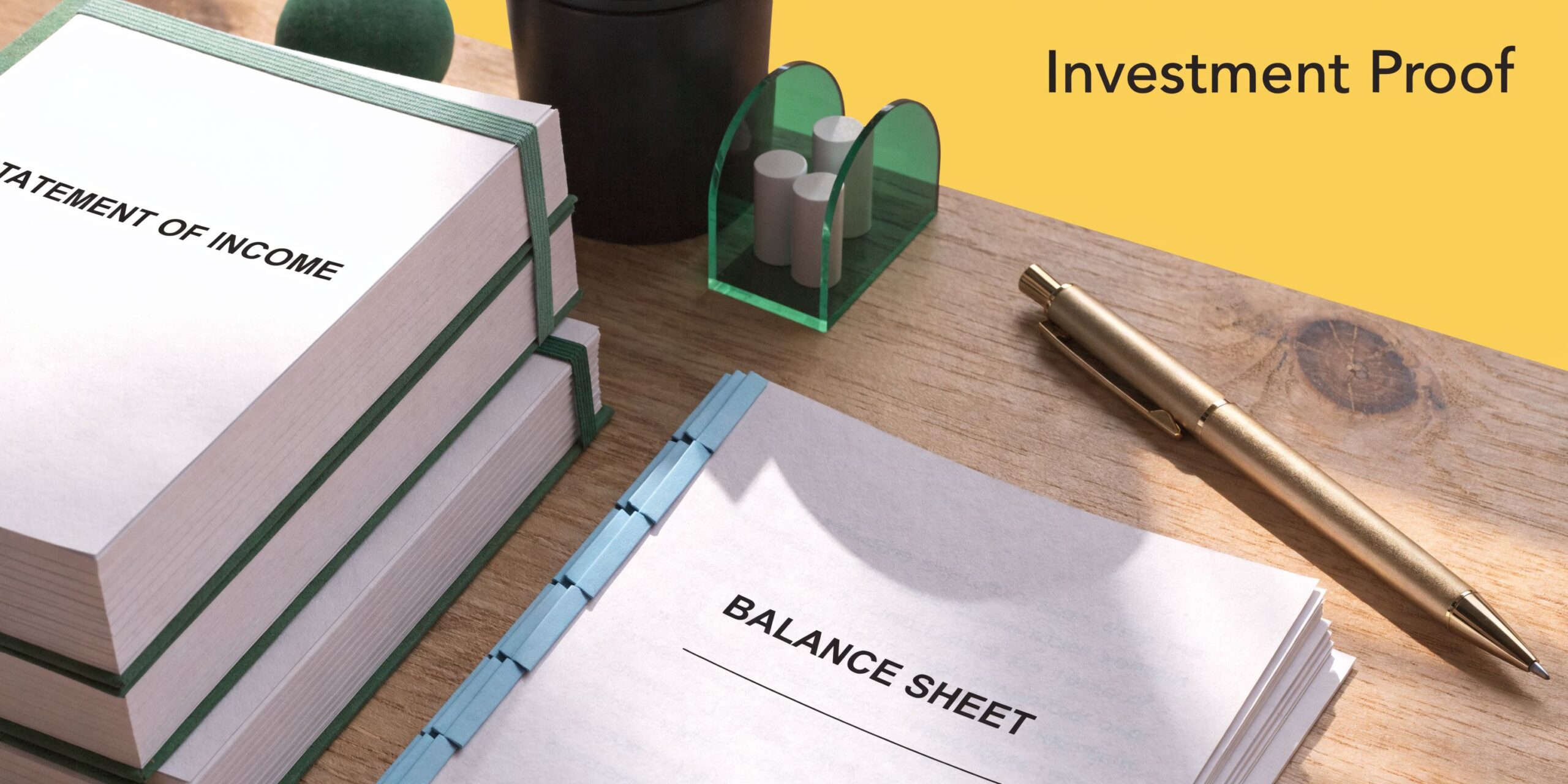 A wooden office desk featuring stacks of income statements and a balance sheet document with a gold pen.