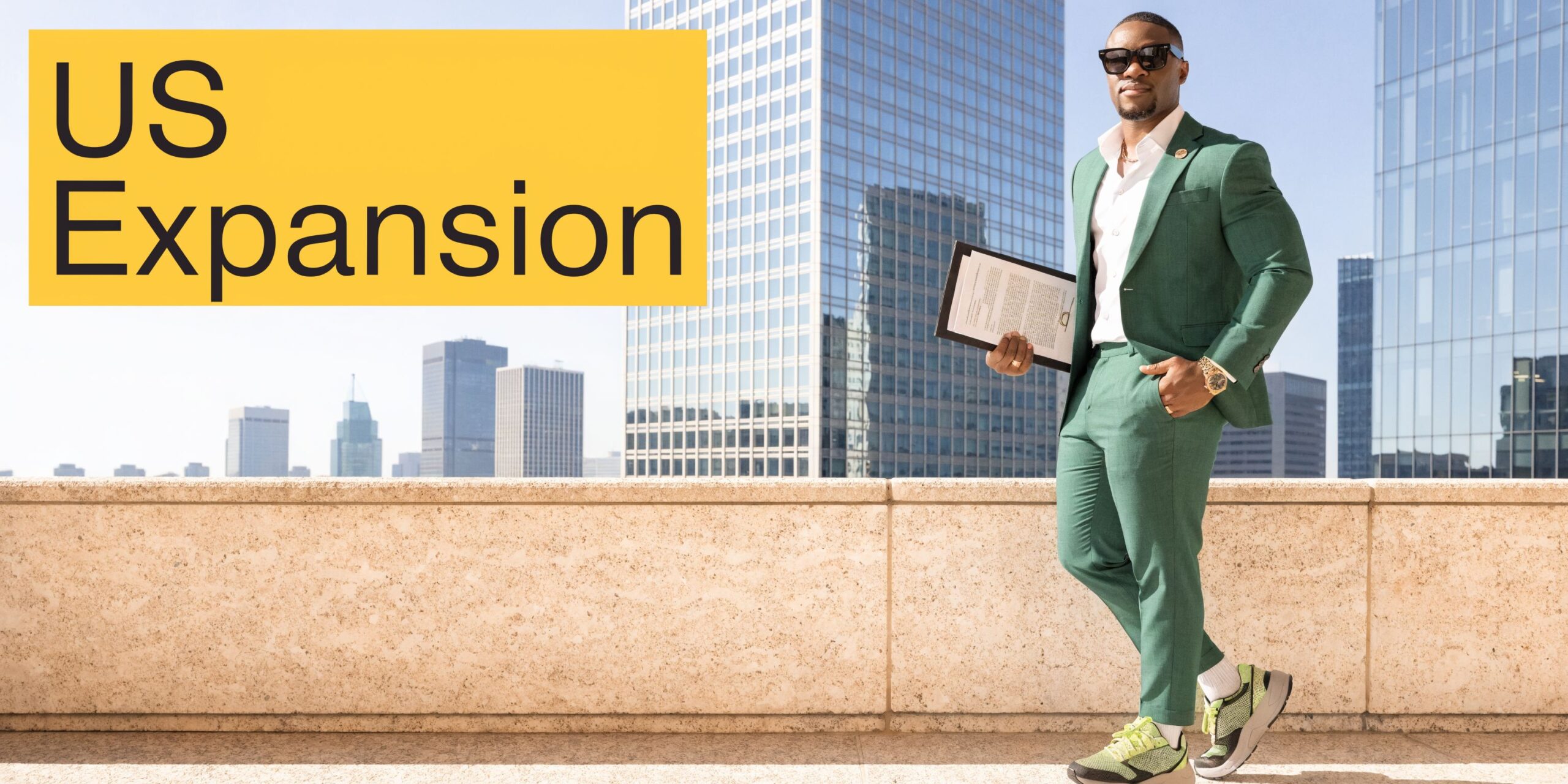 A professional man in a green suit and sneakers holding a business document on a rooftop.