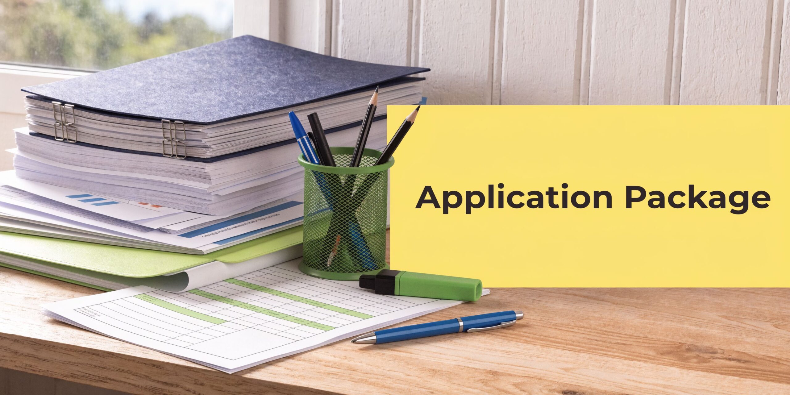 A stack of documents and a pen holder on a wooden desk with a yellow note.