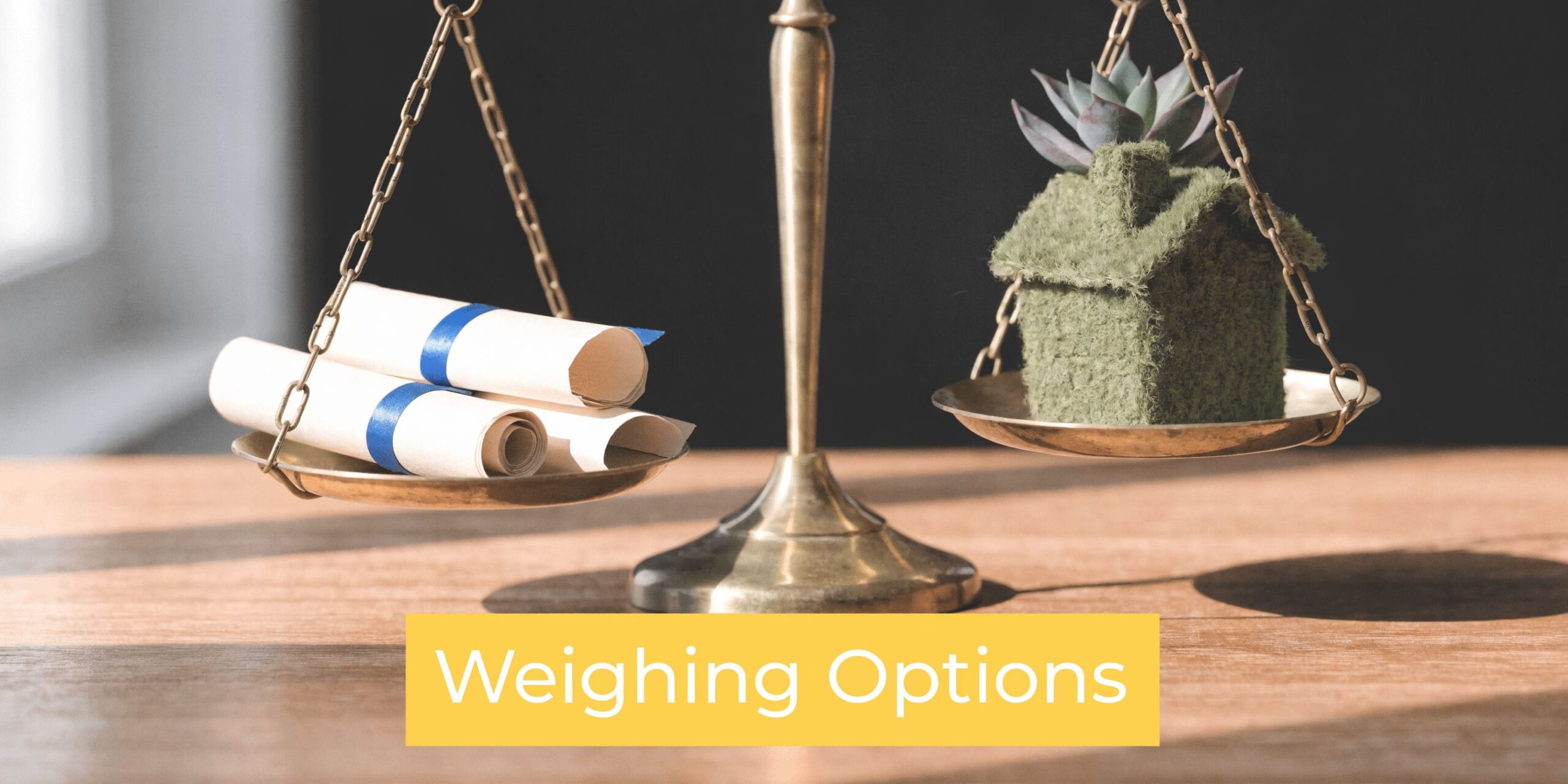 A brass scale balancing rolled legal diplomas on one side and a model house on the other.