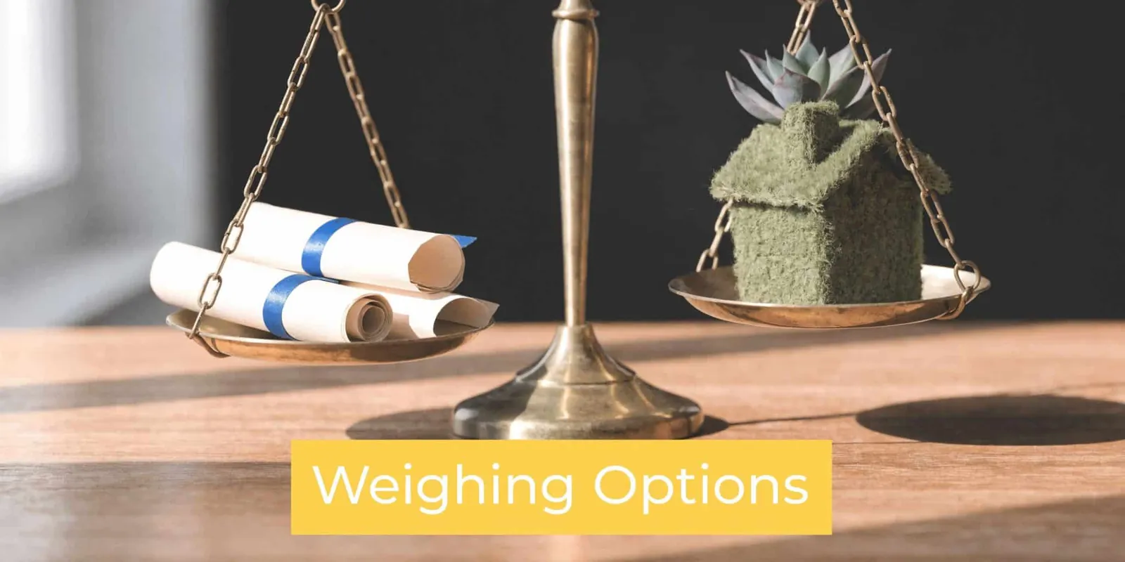 A brass scale balancing rolled legal diplomas on one side and a model house on the other.