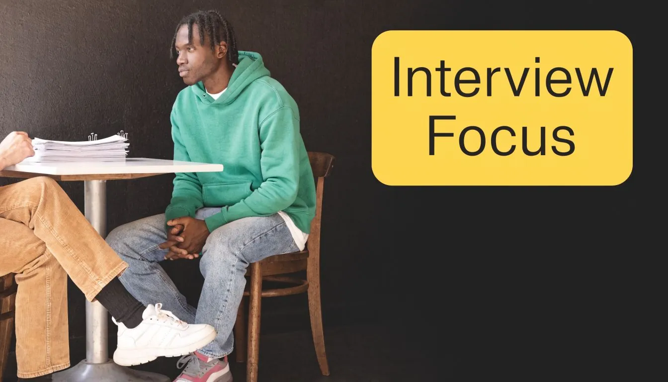 A young man sitting for an interview in a room with a black wall background.