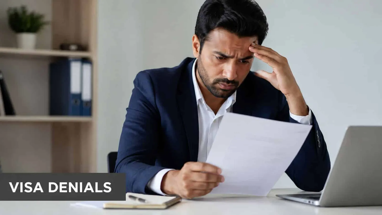 A frustrated businessman sitting at his desk looking at legal documents related to visa denials.