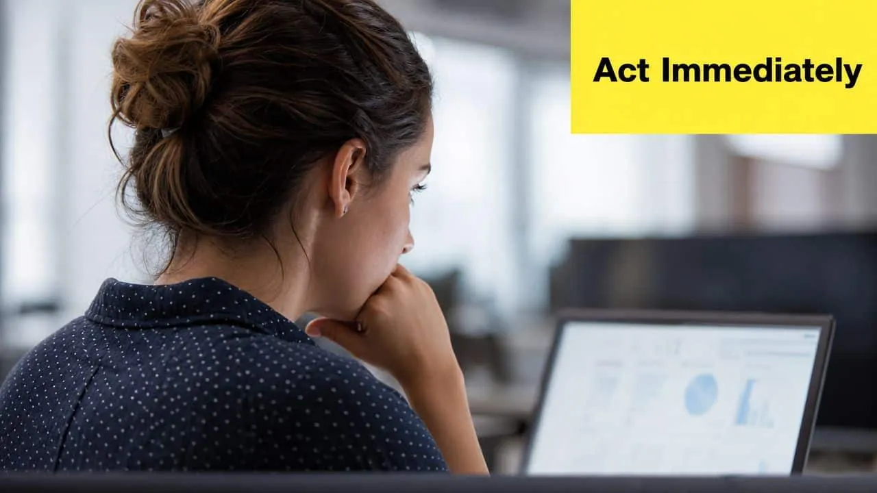 A businesswoman sitting at a desk and reviewing data on a laptop screen with intense focus.